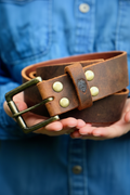 Distressed brown leather belt with brass buckle held in hand